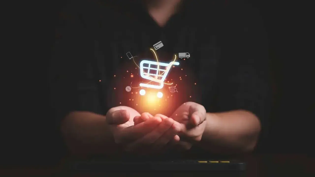 Dłonie trzymające świecący koszyk zakupowy z ikonami symbolizującymi e-commerce: karty kredytowe, telefon, ciężarówka, globus.