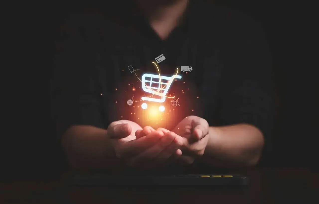 Dłonie trzymające świecący koszyk zakupowy z ikonami symbolizującymi e-commerce: karty kredytowe, telefon, ciężarówka, globus.